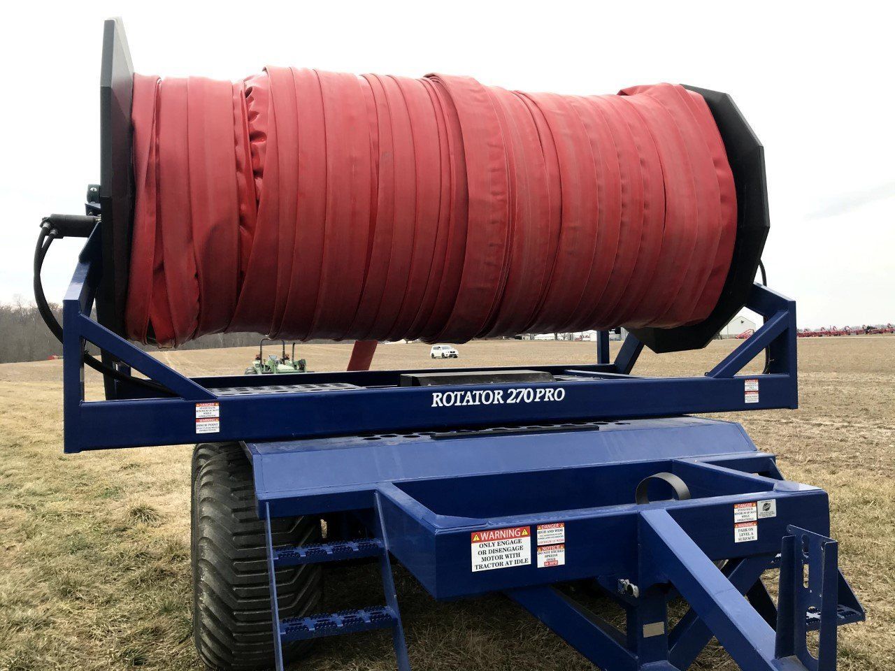 Blue irrigation reel trailer with a large red hose spool on a grassy field
