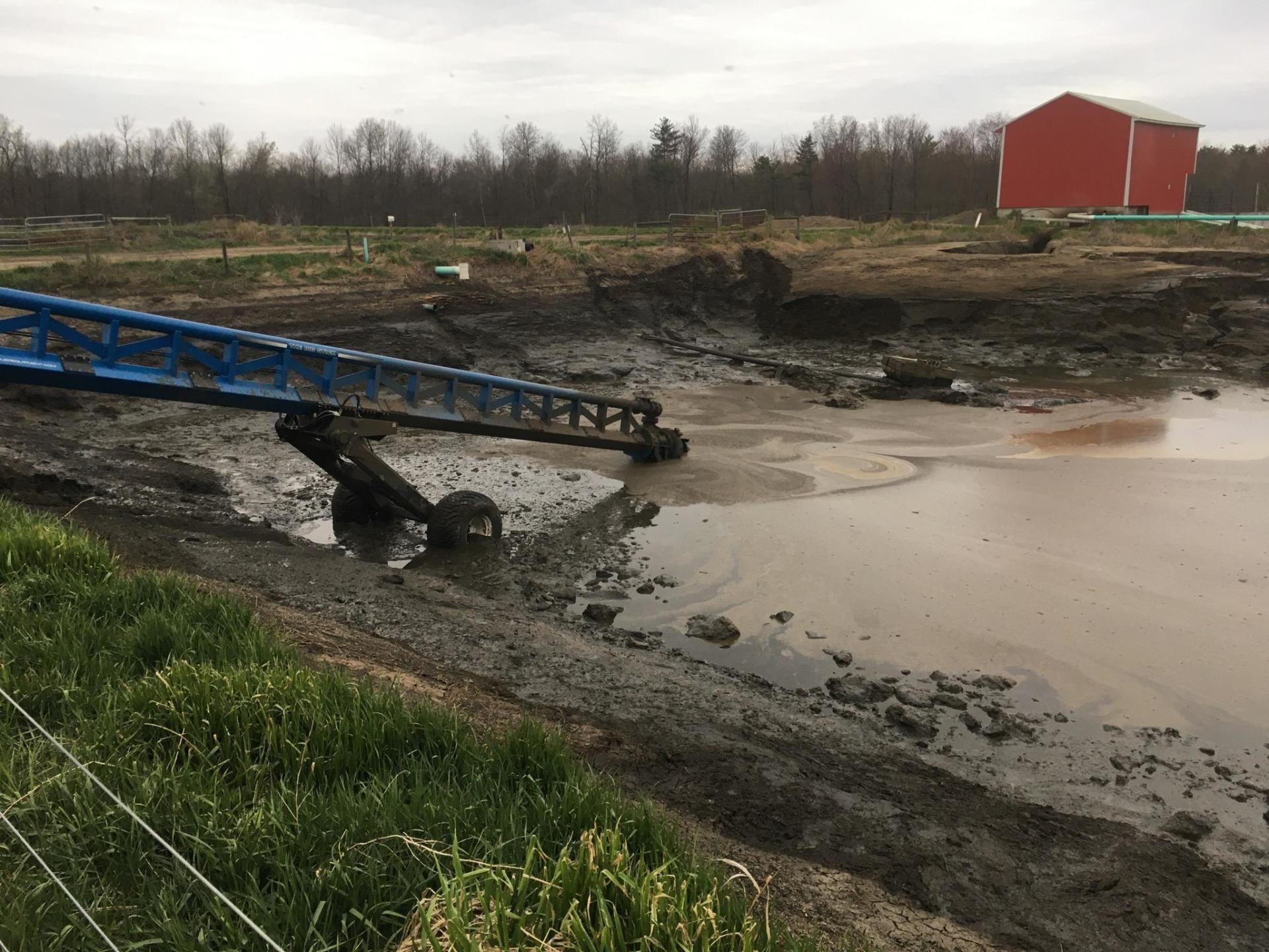 Collapsed blue bridge over muddy creek beside a red barn on a cloudy day