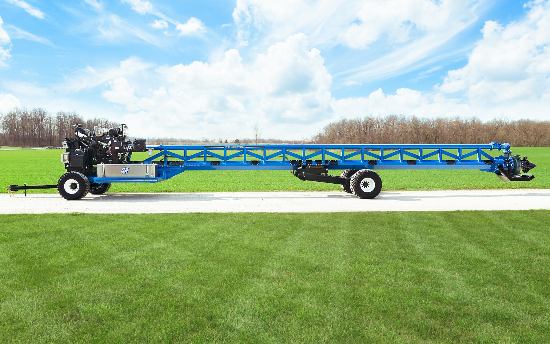 Blue agricultural boom sprayer parked on a road beside a green field under a cloudy sky