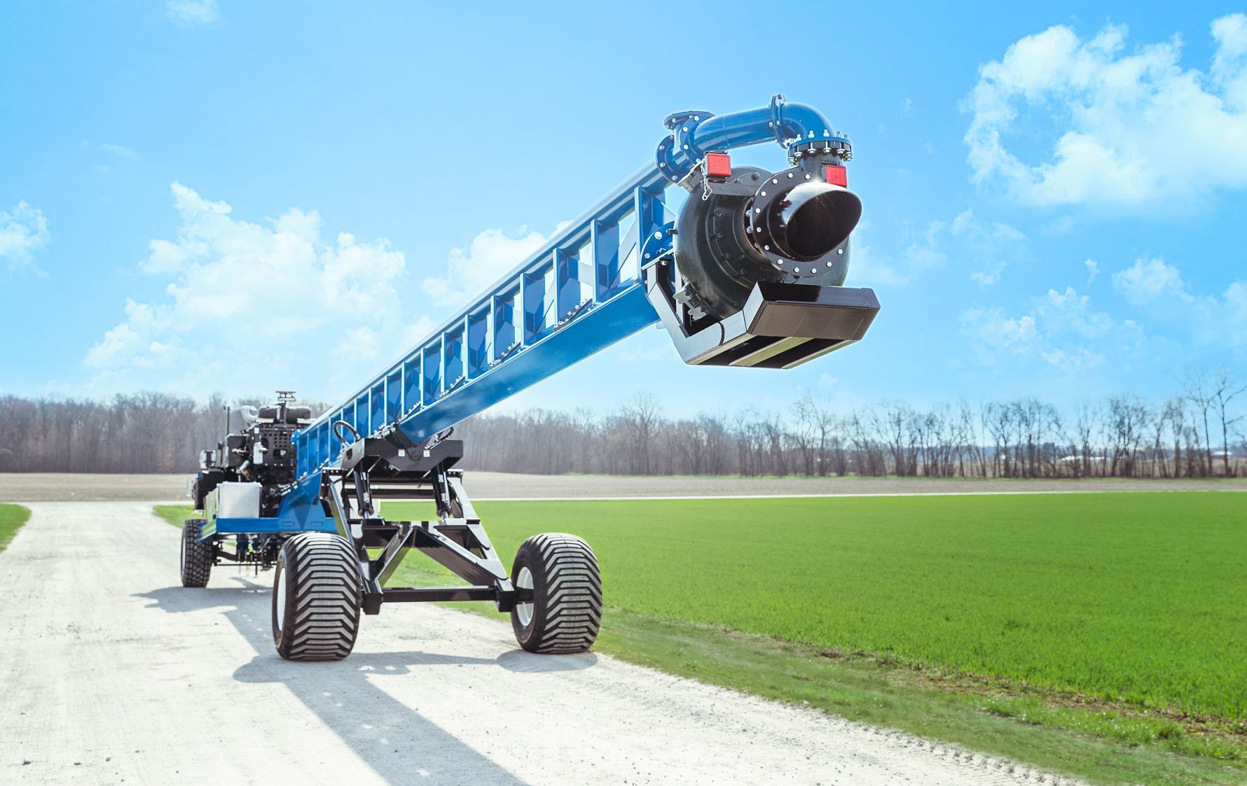 Blue agricultural sprayer on a farm road beside green fields under a clear sky