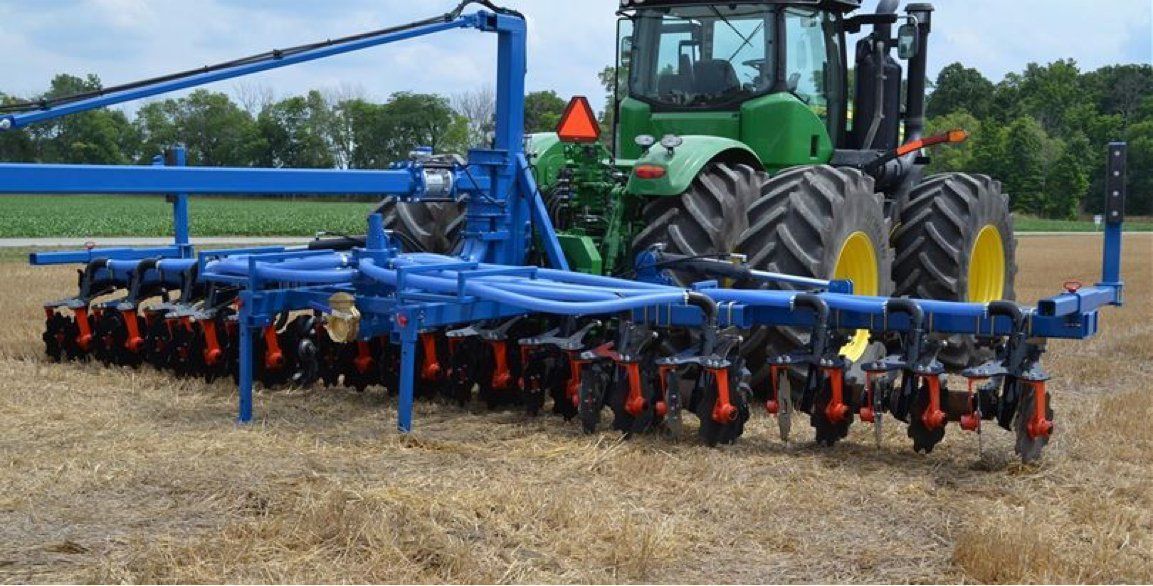 Blue agricultural implement attached to a green tractor working in a field