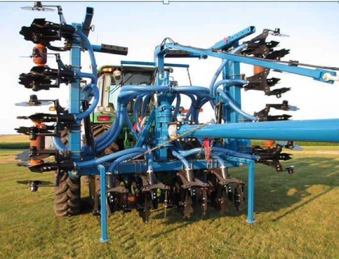 Blue agricultural sprayer machine in a field, with multiple folding arms and nozzles attached.