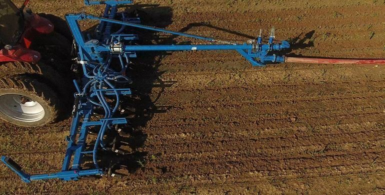 Blue farm tillage implement working soil behind tractor wheel in a field, viewed from above