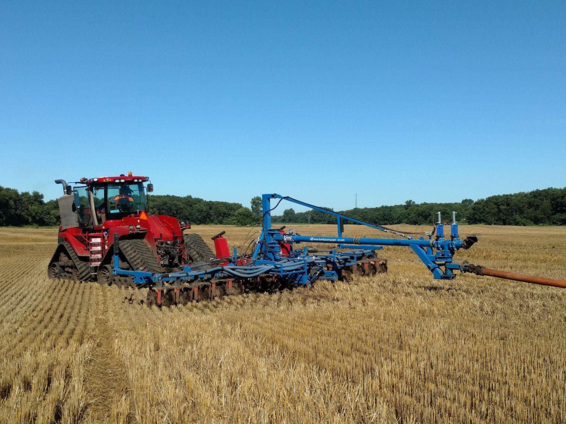 Red tractor pulling blue farm equipment across a harvested field under a clear sky