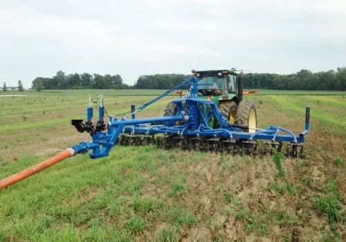 Blue farm tractor towing a plow across a green field