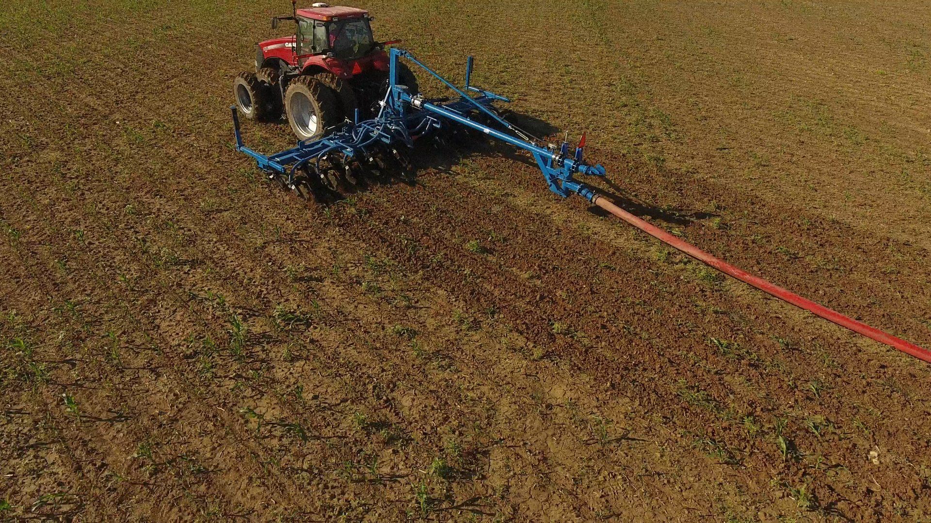 Red tractor spraying a field with a blue agricultural boom
