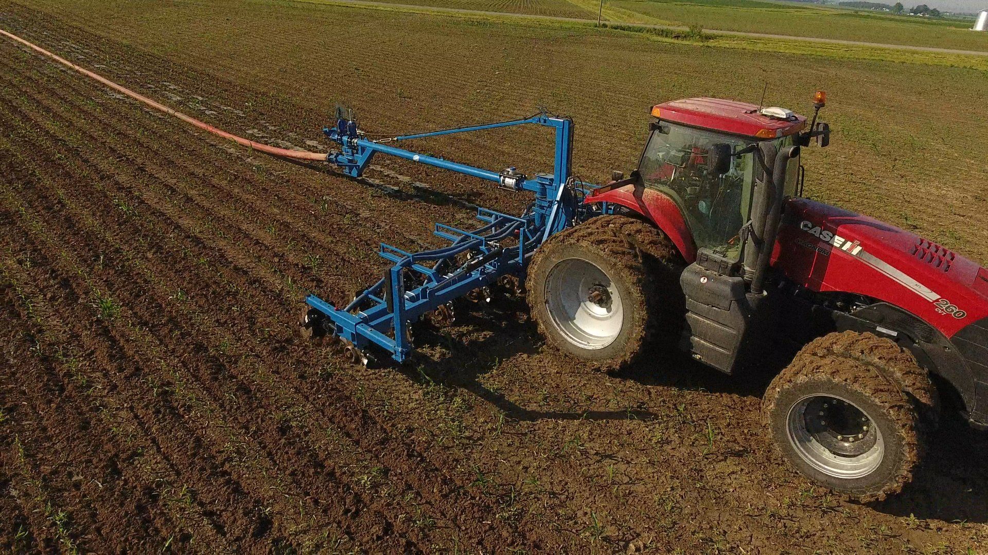Red tractor pulling a blue field implement across a crop field