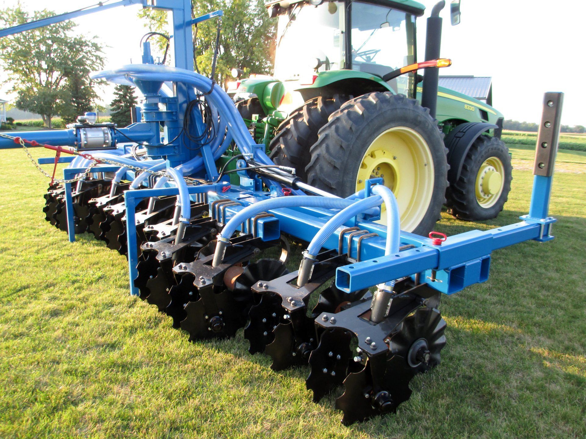 Blue agricultural tillage implement attached to a tractor on a grassy field