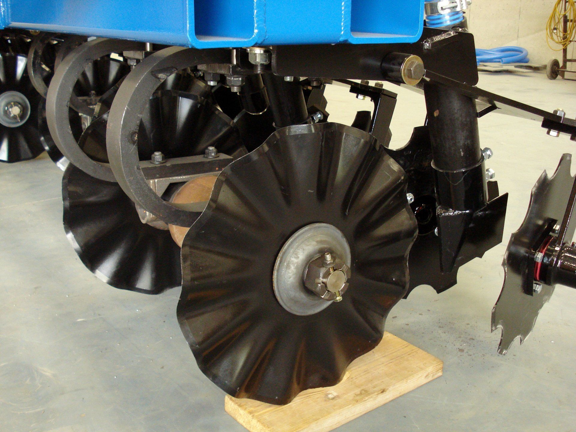 Close-up of a blue farm machine wheel with black tines on a wooden block in a workshop