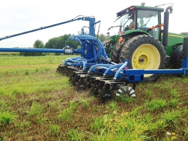 Blue farm implement on a green field beside a green tractor, spraying or cultivating crops