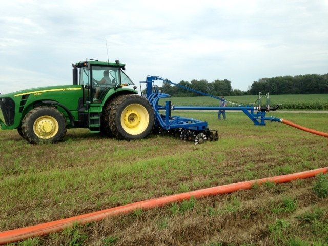 Green tractor with blue farm irrigation equipment in a grassy field under cloudy sky