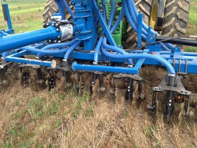 Blue farm tillage implement working in a field, with multiple discs cutting soil and dry grass