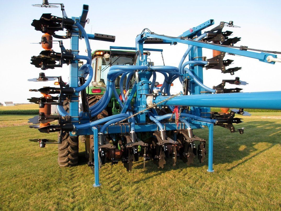 Blue agricultural implement with multiple discs and wheels on a grassy field under a clear sky