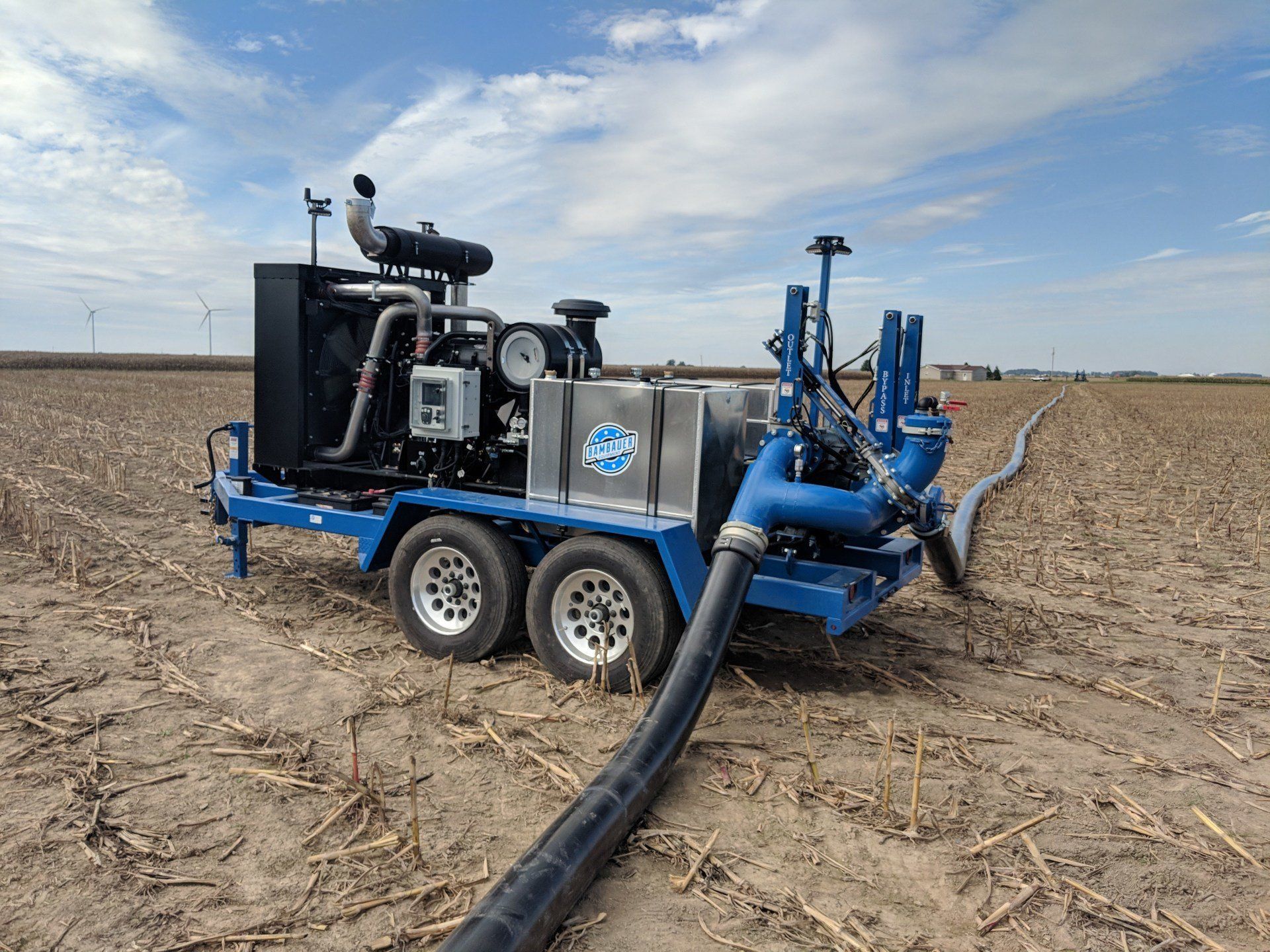 Blue irrigation pump trailer with large black hose in a harvested field under a cloudy sky