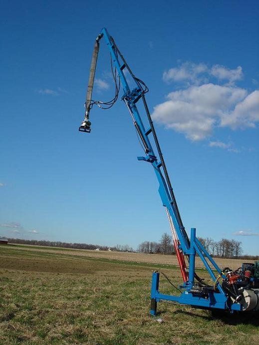Blue hydraulic crane arm lifting a tool over a field under a clear blue sky