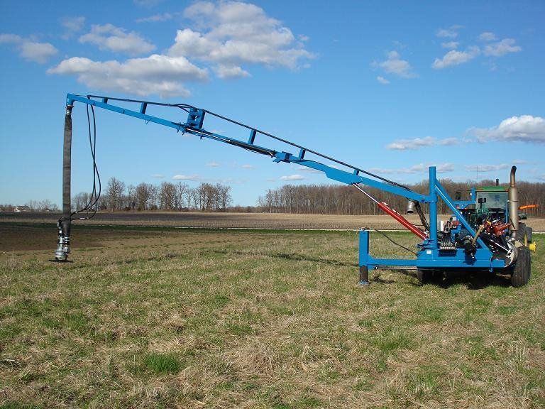 Blue irrigation boom machine spraying water over a grassy field under a clear sky