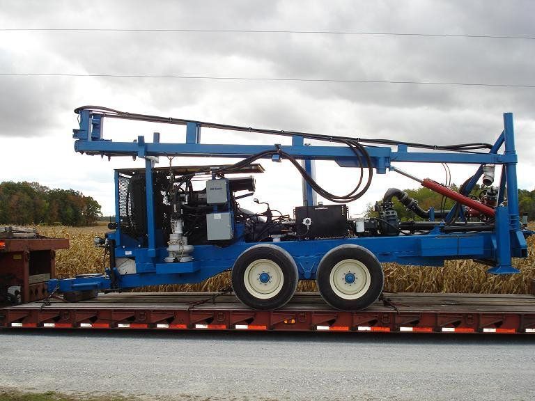 Blue drilling rig on a trailer, parked outdoors under a cloudy sky.