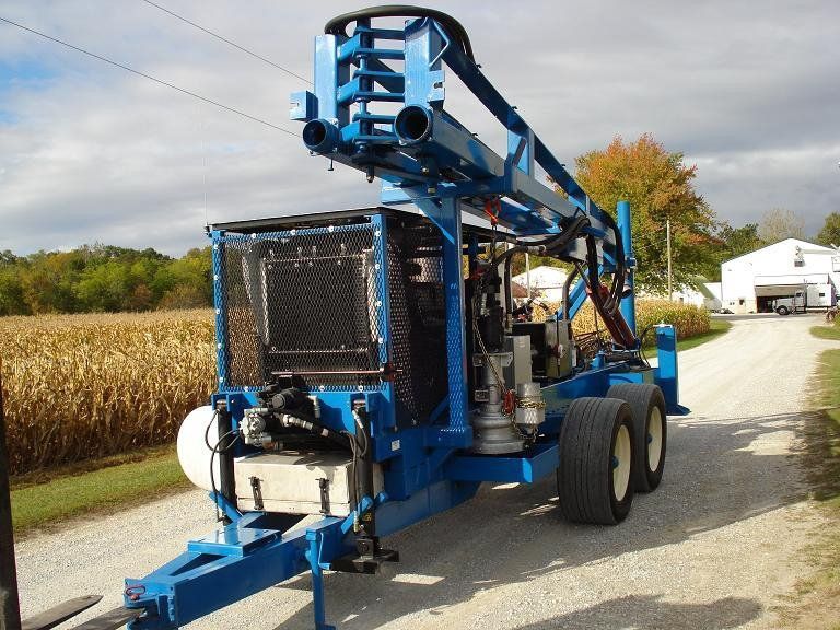 Blue agricultural machine parked on a rural road beside a cornfield and trees