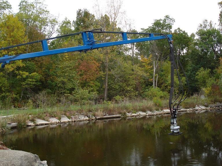 Blue crane lifting a small object from a calm river beside a rocky, tree-lined bank