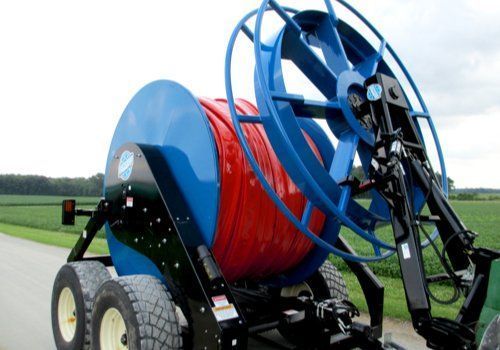 Blue farm irrigation reel cart with red hose in a field