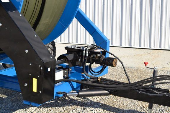 Blue agricultural machine hitch with hoses and cables beside a corrugated metal building.