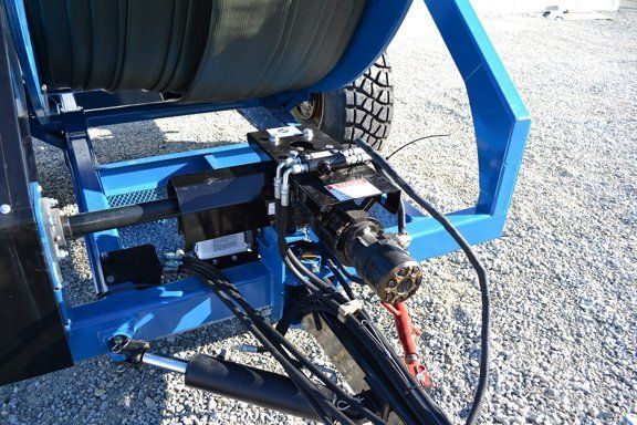Blue-framed mechanical device mounted outdoors on gravel, with wheels and cables visible under a seat-like cover