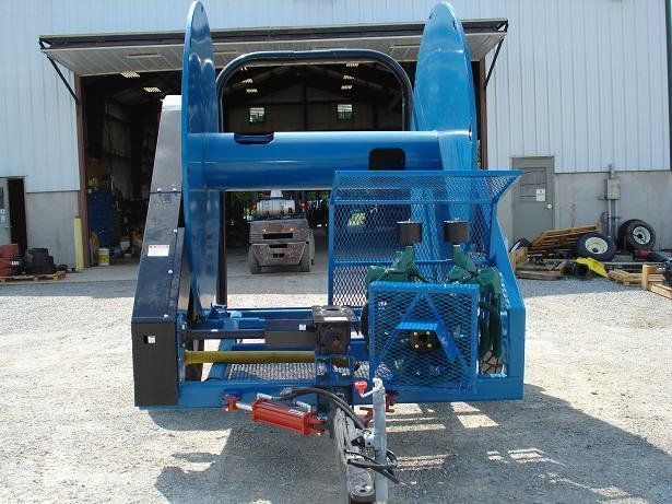 Blue skid-steer loader in a warehouse, with a front-mounted attachment and gravel ground.