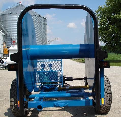 Blue agricultural machine with large rear wheels parked on a farm lane beside grain silos