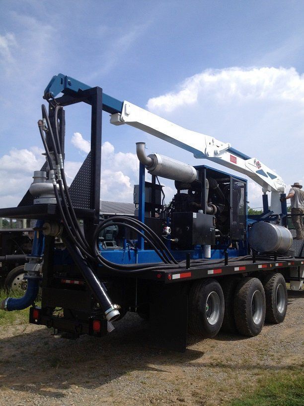 Black utility truck with crane and hoses parked outdoors on gravel under a blue sky