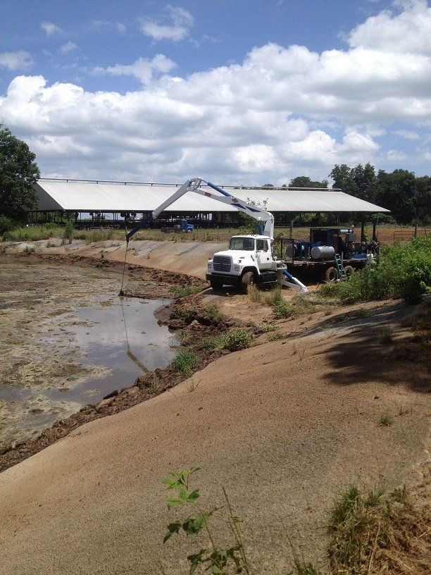 Truck on muddy construction site beside a large white building under a cloudy sky