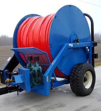 Blue hose reel trailer with large red hose on a rural roadside