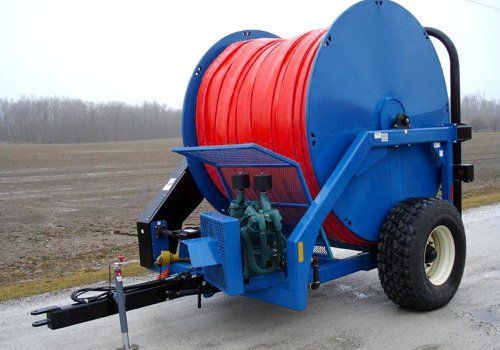 Blue hose reel trailer with red hose on a farm road