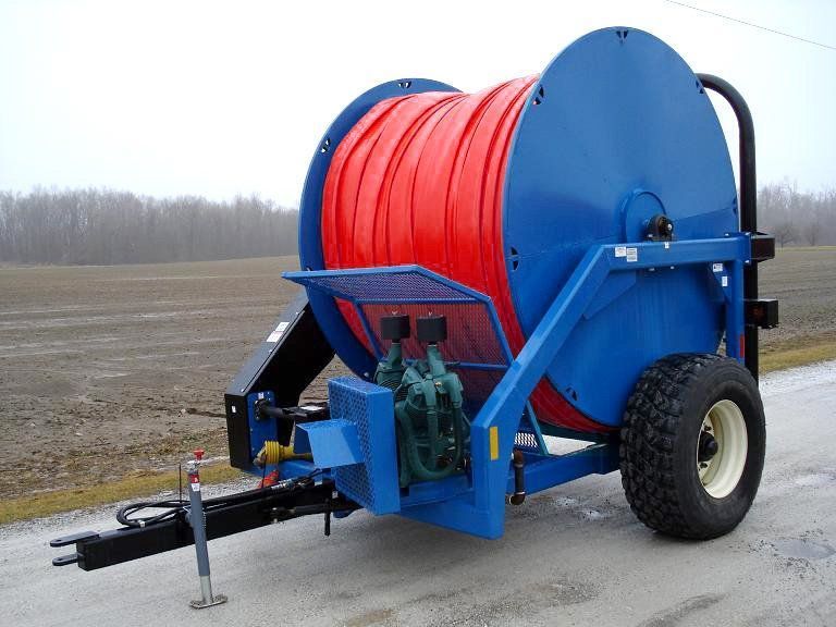 Blue hose reel trailer with a large red hose and black tires on a field