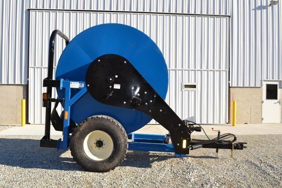 Blue industrial reel trailer with large hose spool parked on gravel in front of a metal building