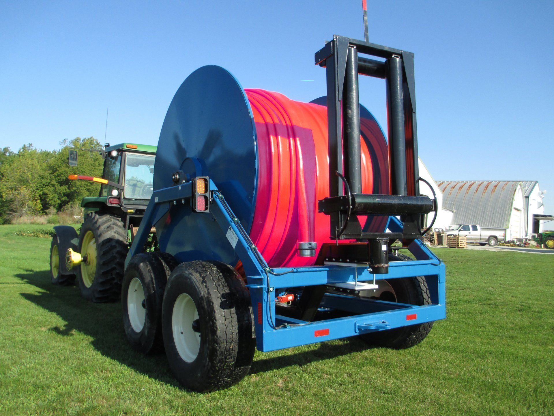 Blue farm trailer with large red hose reel being towed across a grassy field