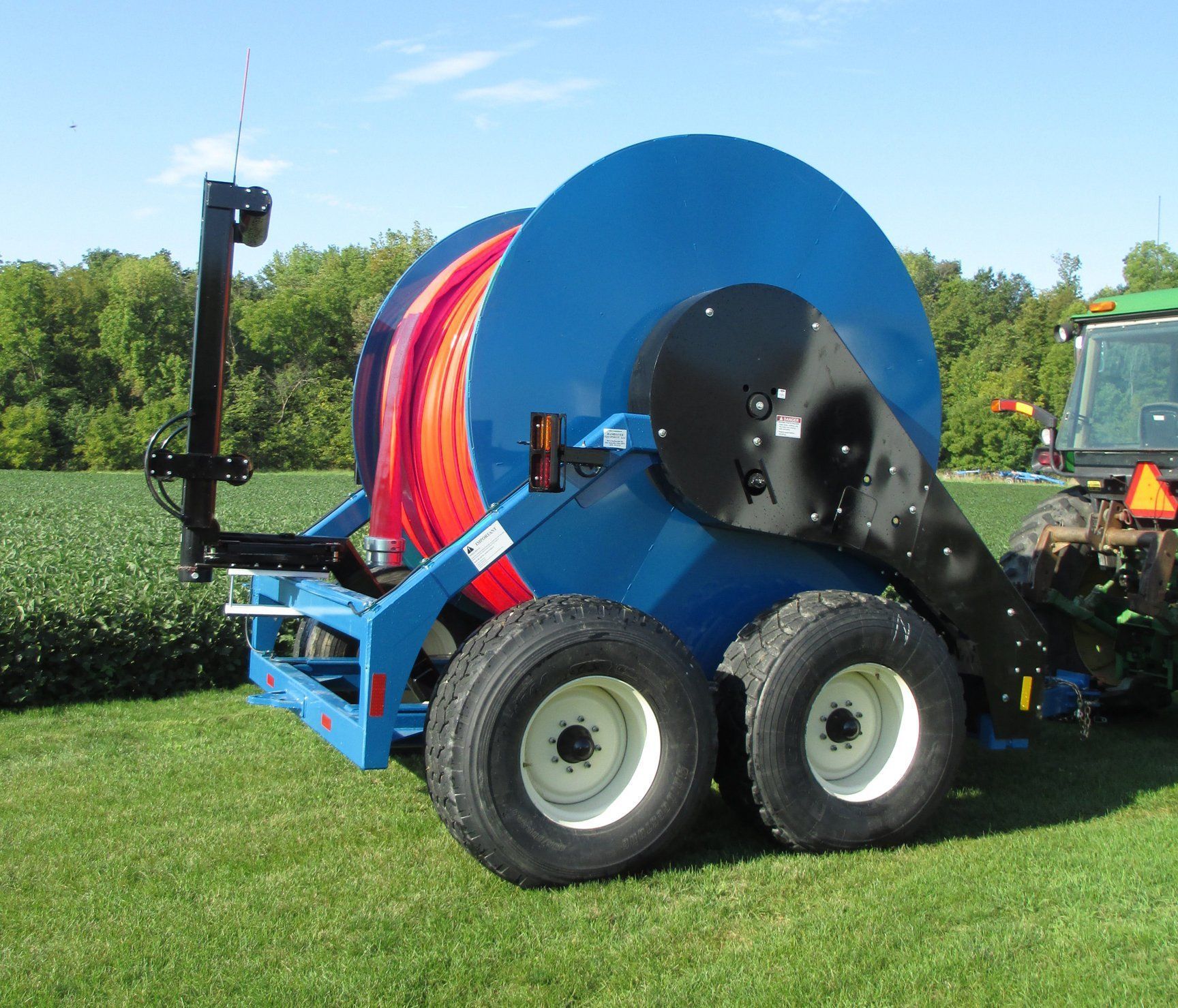 Blue hose reel trailer with red hose on a grassy field, attached to a tractor