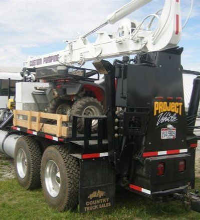Black pickup truck hauling an ATV and white boom lift on a trailer with “Project Access” signage.