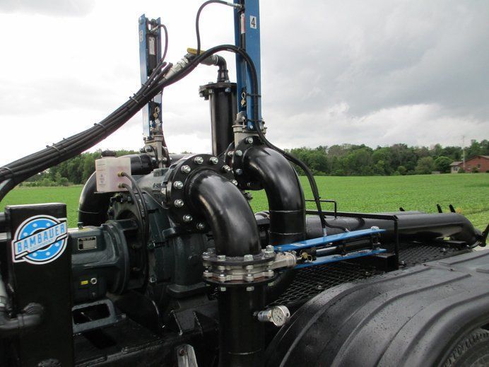 Heavy black agricultural machinery with blue hydraulic parts in a green field under cloudy sky