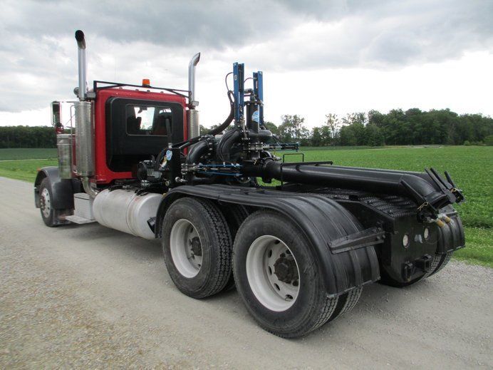 Red semi truck chassis with exposed frame parked on a road beside green fields