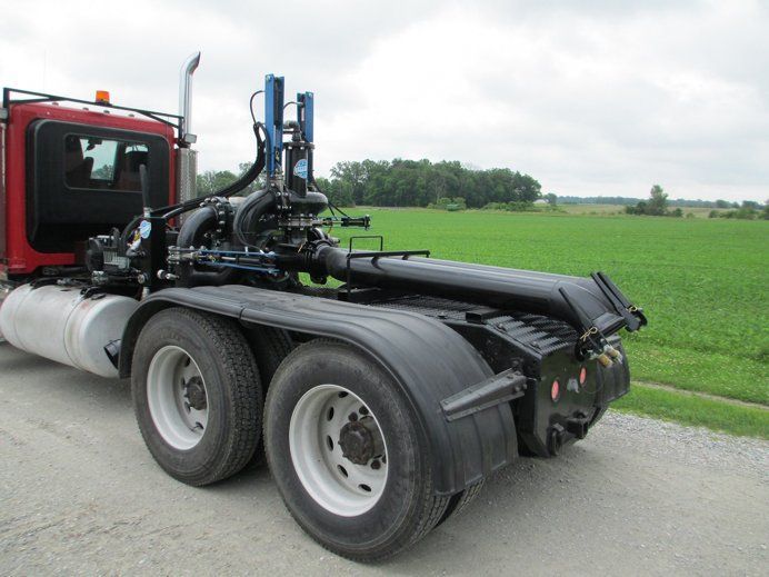 Red semi truck chassis with dual rear wheels parked beside a green field