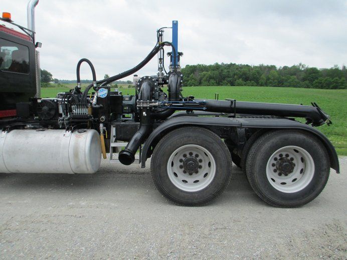 Black truck with a large mounted industrial tank and machinery on a gravel road, side view