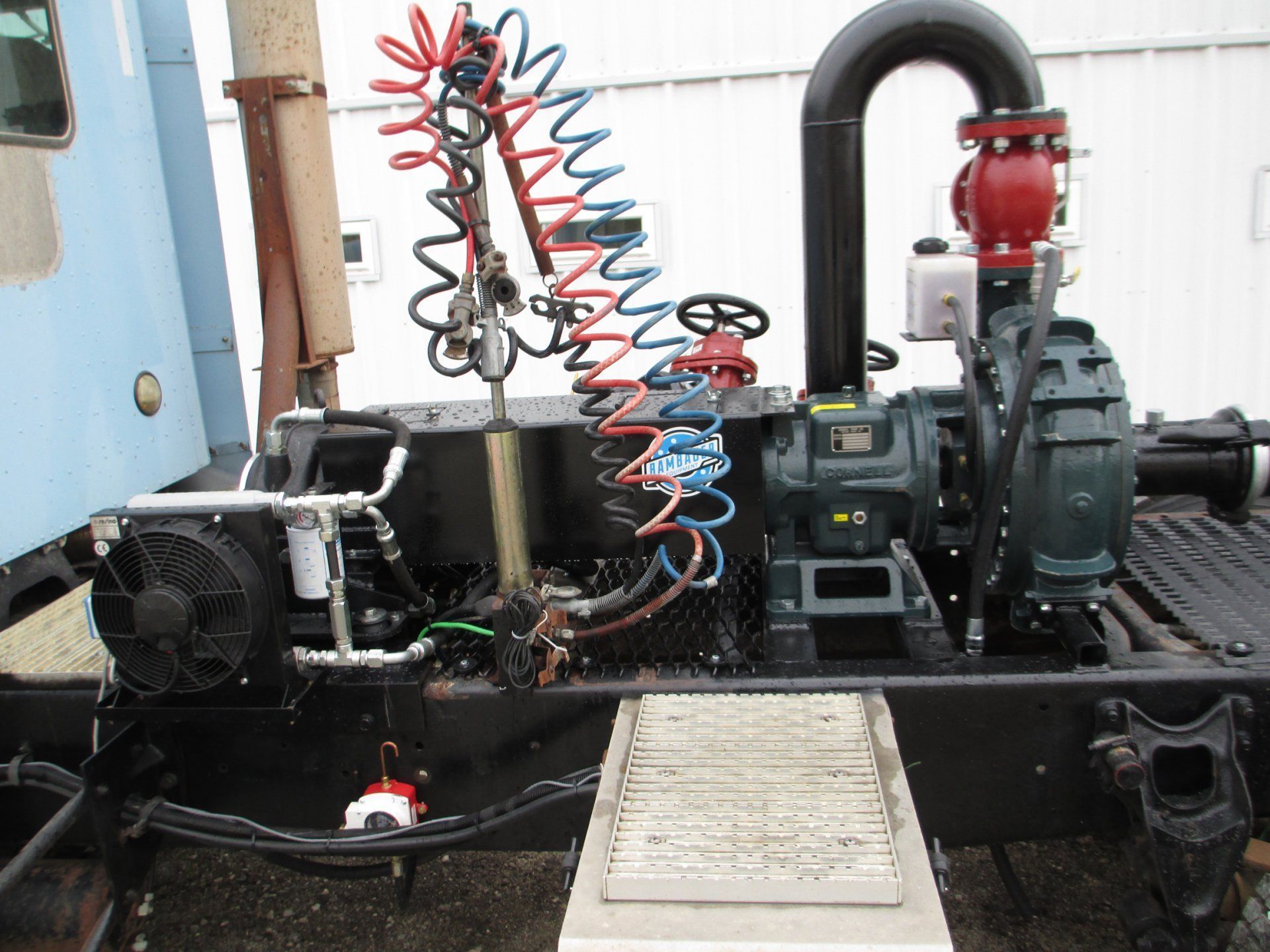 Industrial pump and compressor setup with black hoses, red and blue coils, and a control panel on a metal platform