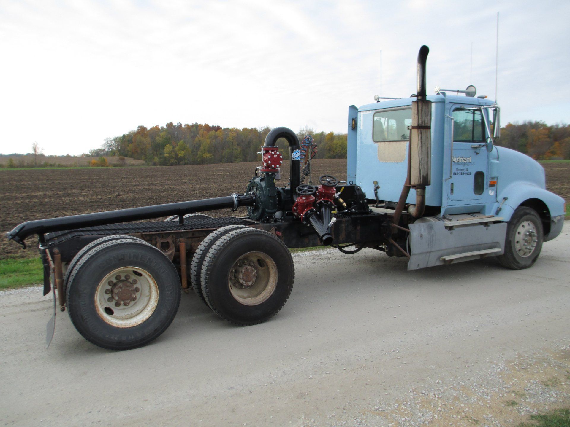 Black truck chassis with dual rear wheels parked on a gravel road under a cloudy sky.