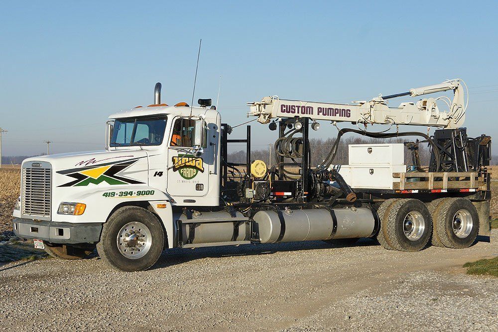White drilling truck on gravel with equipment mounted on back under a clear sky
