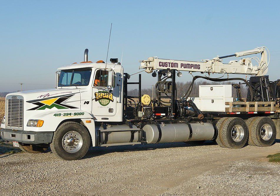White cement truck with boom arm parked on gravel lot under clear sky