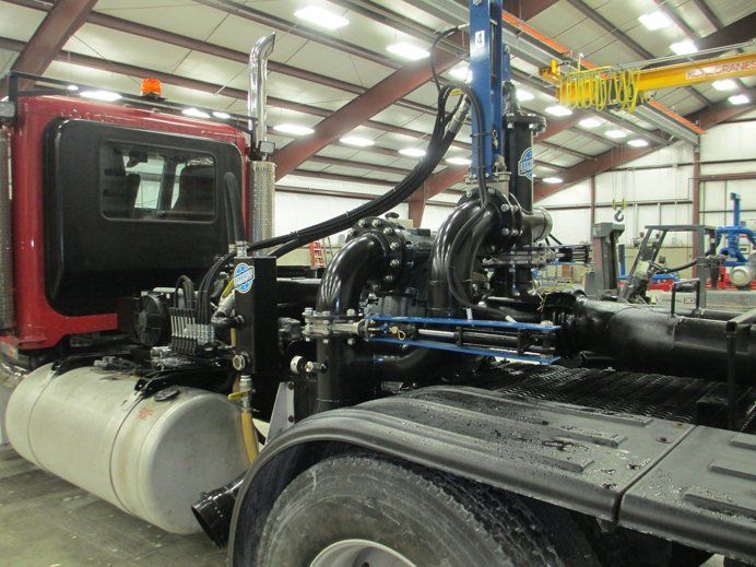 Red semi-truck in a garage with a large black mechanical rig and white fuel tank attached