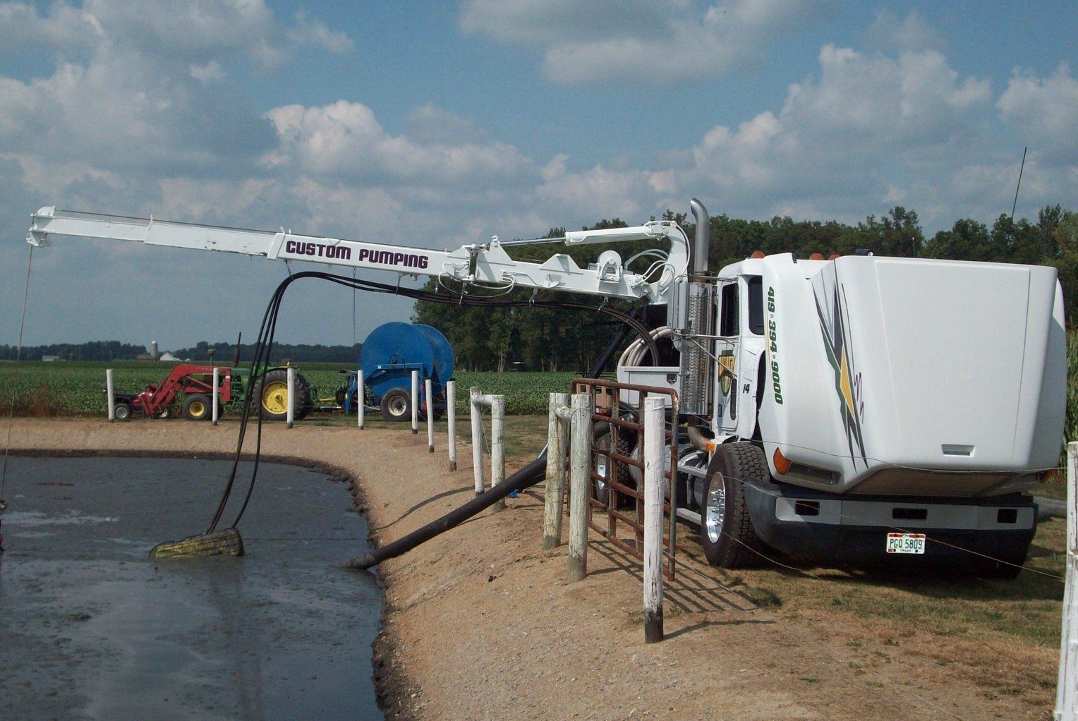White utility truck with boom arm working beside a water canal on a dirt road under a cloudy sky