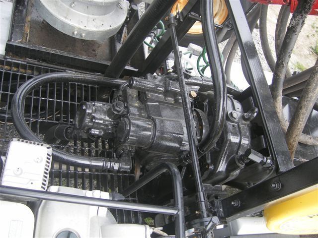 Close-up of a black mechanical engine or pump assembly with hoses and metal tubing in a industrial setting