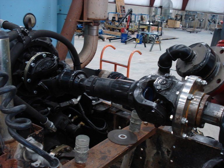 Industrial pump and pipe assembly in a workshop, with black machinery and metal tubing on a concrete floor