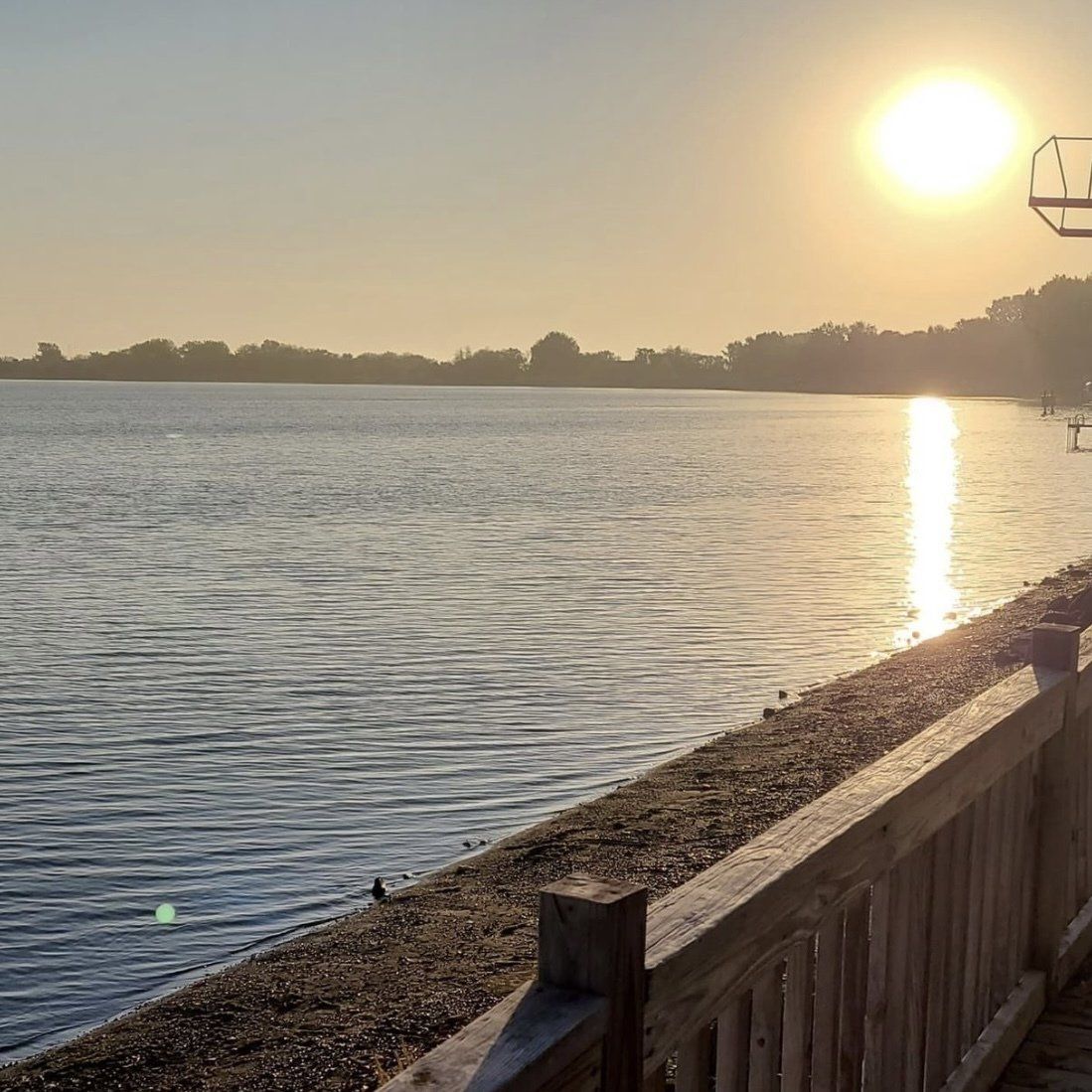The sun is setting over a lake with a wooden fence in the foreground